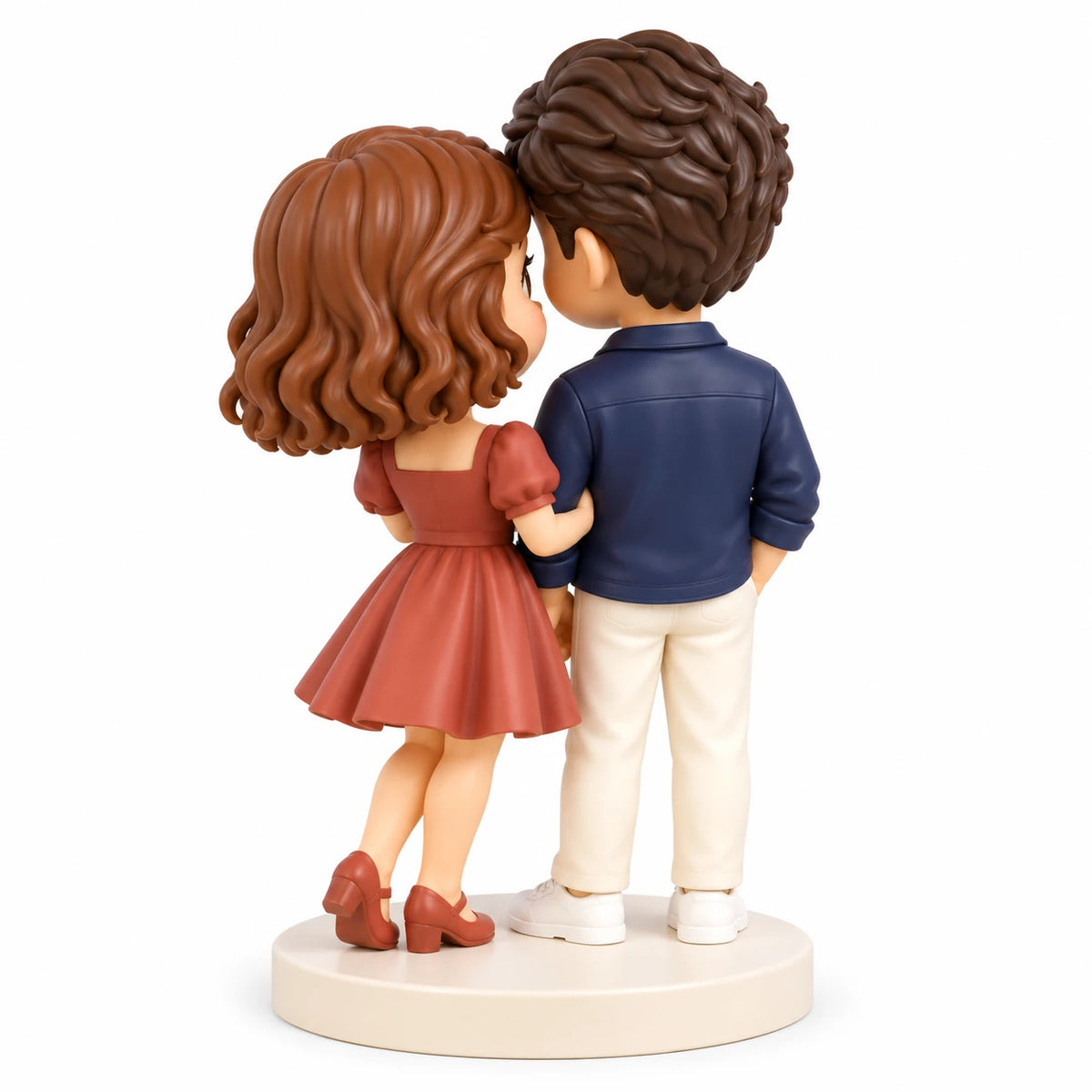 Vue arrière de trois quarts d’un couple chibi peint pour un anniversaire sur un socle crème commun, avec cheveux bruns sculptés, surchemise bleu marine, pantalon crème et robe terre cuite.
